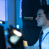 IT helpdesk technician assisting a remote employee while reviewing a support request on computer monitors.