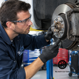 Qualified mechanic checking brake components on a vehicle raised inside an automotive service workshop.