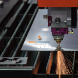 Laser-cut steel panels, bent metal brackets and welded components displayed on a sheet metal fabrication workbench.